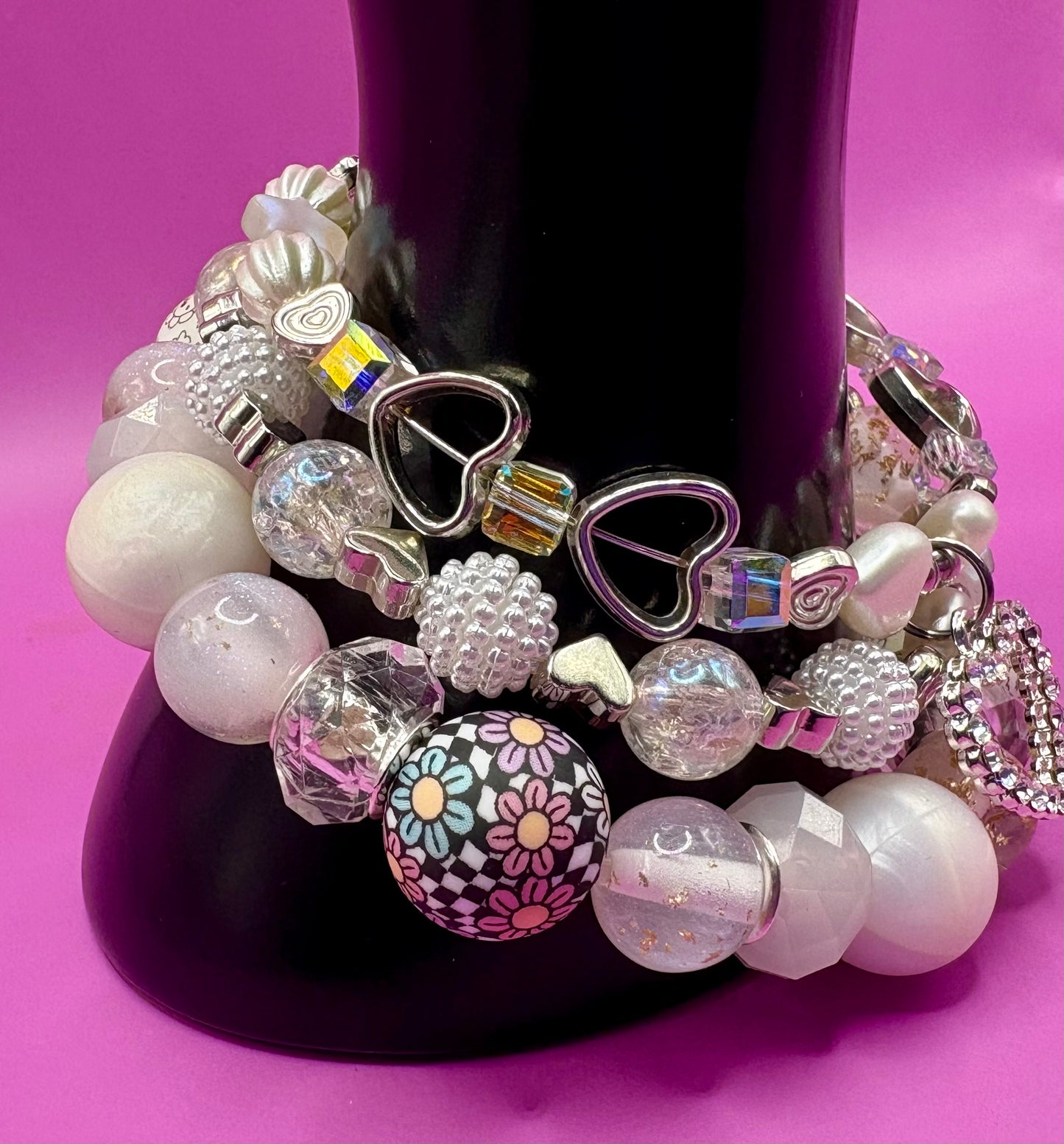 Handmade beaded charm bracelets stacked together, showcasing unique designs and vibrant colors, perfect for adding a personalized touch to any jewelry collection. white and silver hear pendant
