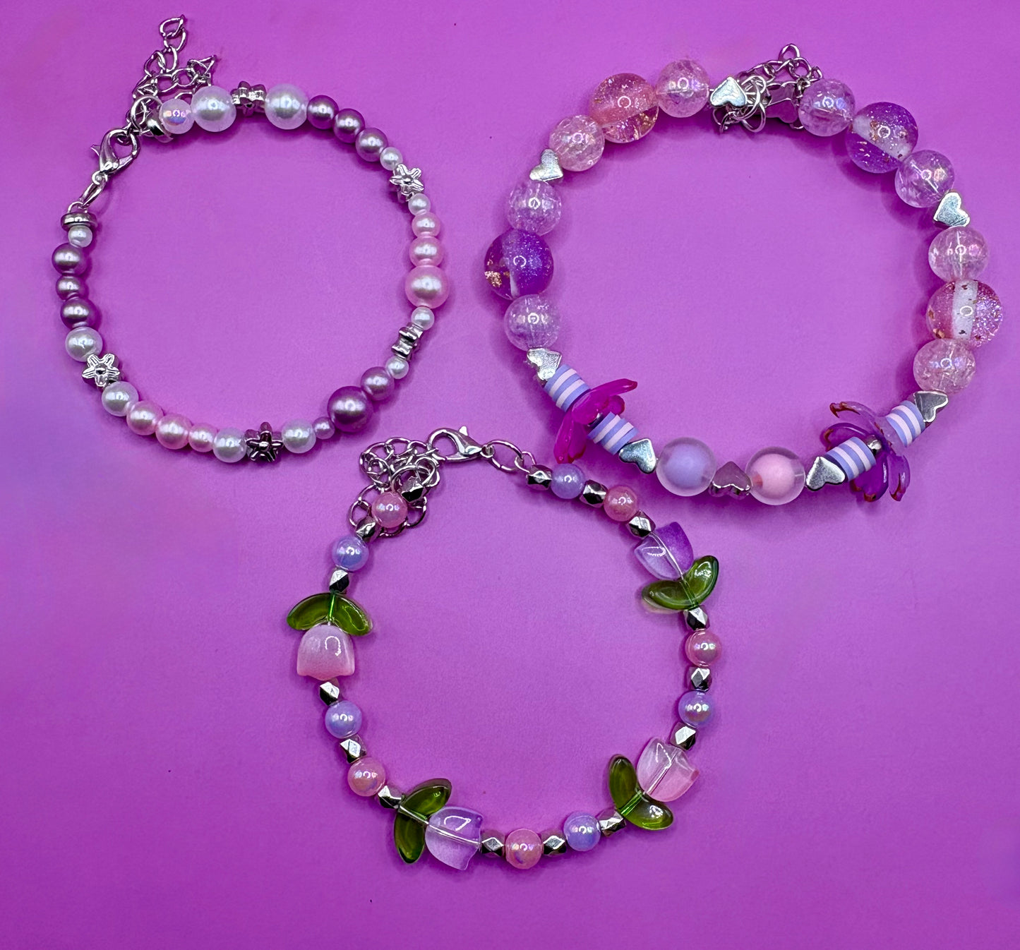 Handmade beaded charm bracelets stacked together, showcasing unique designs and vibrant colors, perfect for adding a personalized touch to any jewelry collection. purple flower tulip petals pink
