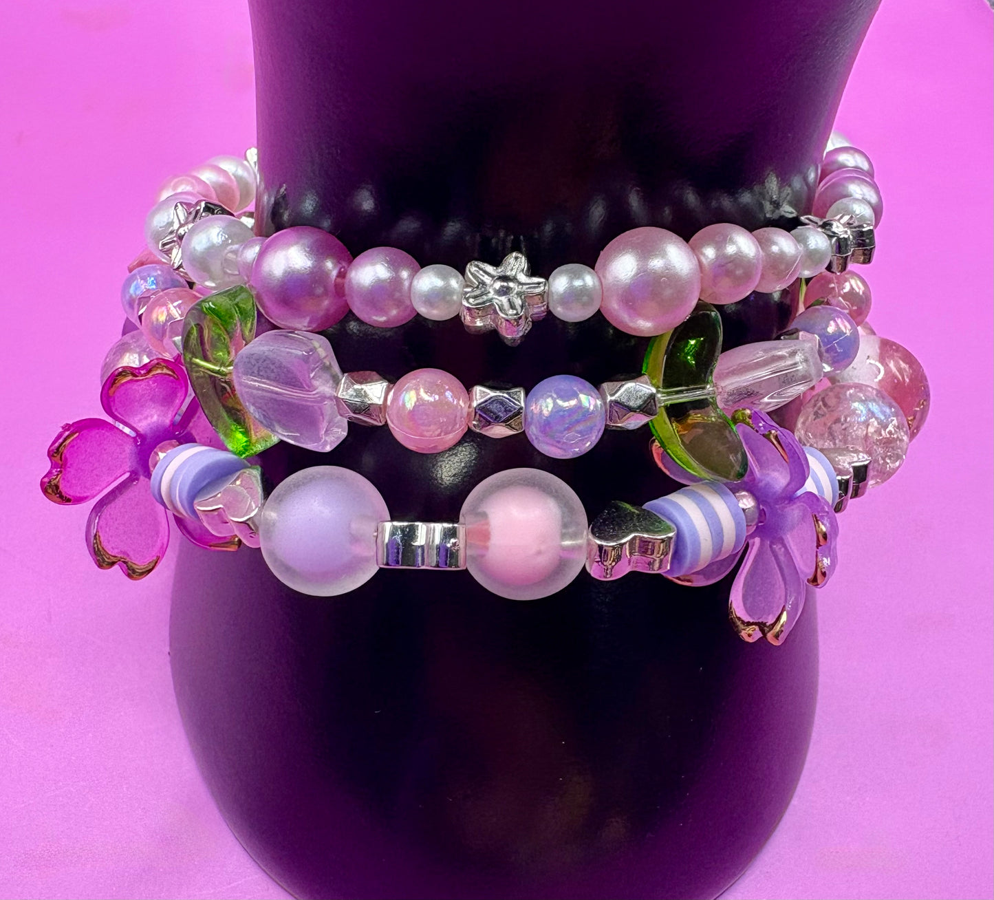 Handmade beaded charm bracelets stacked together, showcasing unique designs and vibrant colors, perfect for adding a personalized touch to any jewelry collection. purple flower tulip petals pink