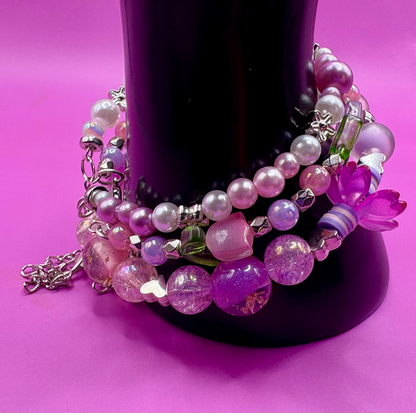 Handmade beaded charm bracelets stacked together, showcasing unique designs and vibrant colors, perfect for adding a personalized touch to any jewelry collection. purple flower tulip petals pink