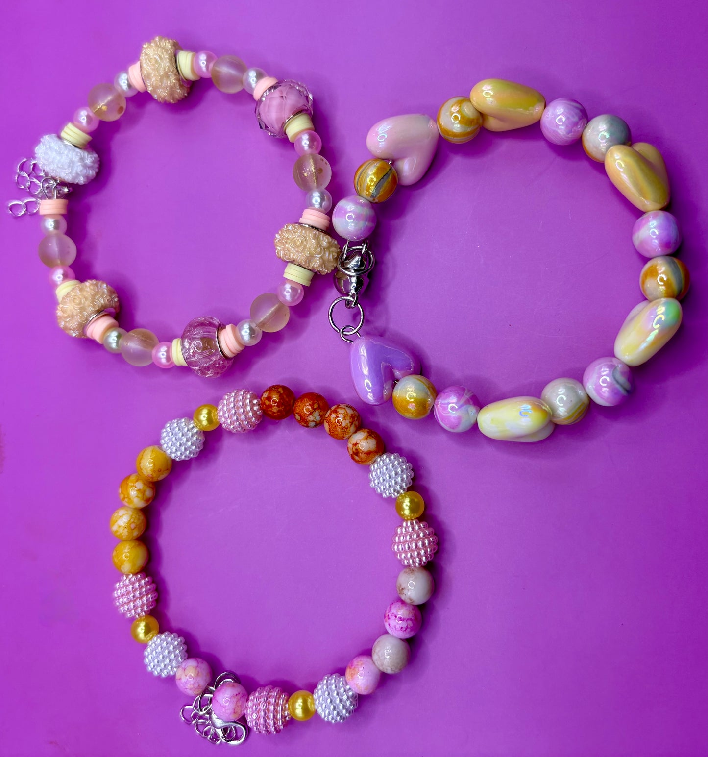 Handmade beaded charm bracelets stacked together, showcasing unique designs and vibrant colors, perfect for adding a personalized touch to any jewelry collection. yellow floral love hearts pink orange