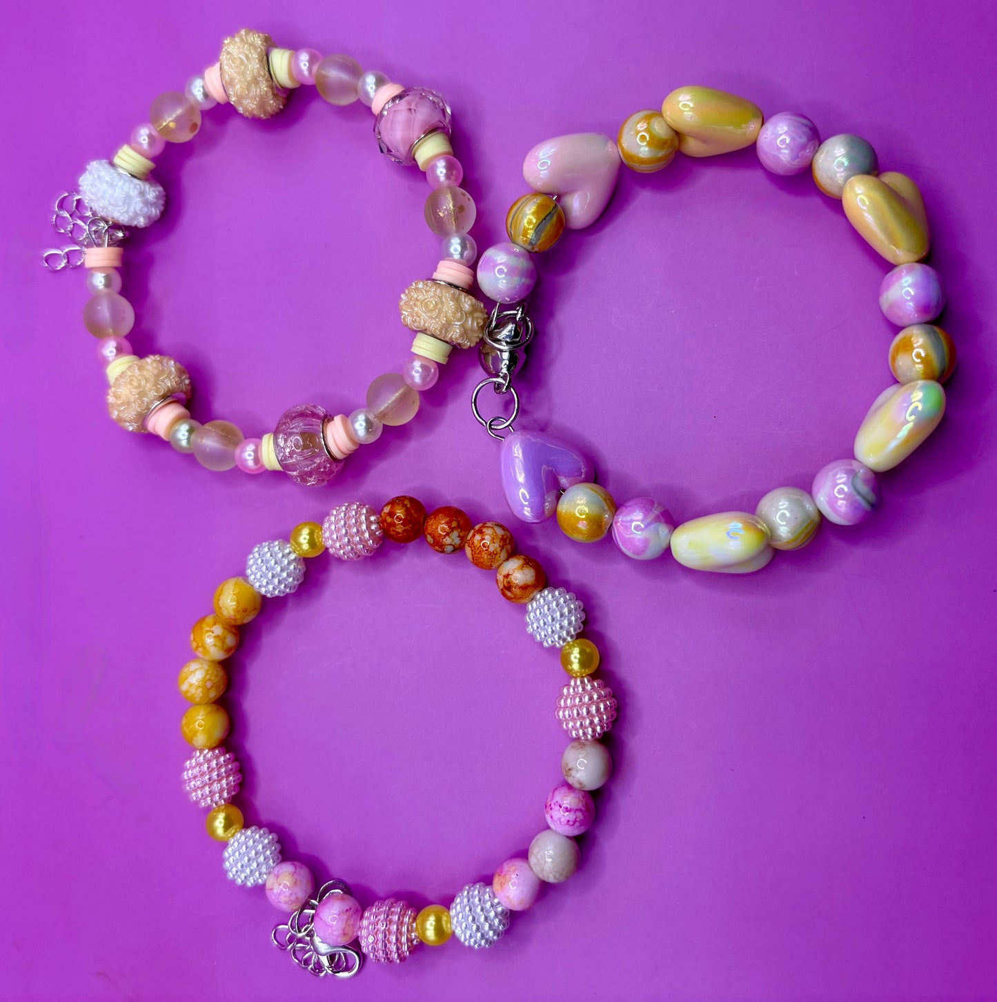 Handmade beaded charm bracelets stacked together, showcasing unique designs and vibrant colors, perfect for adding a personalized touch to any jewelry collection. yellow floral love hearts pink orange