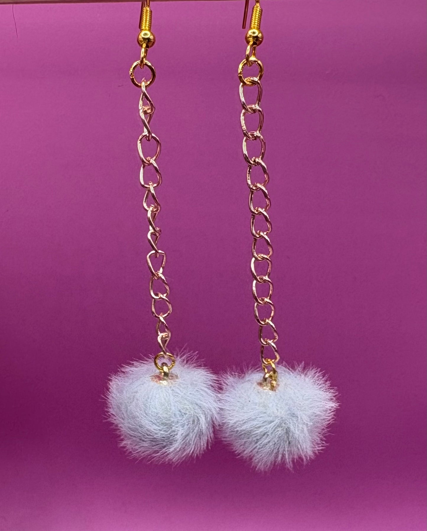 Trendy long dangly drop earrings with fluffy pom pom embellishments, perfect for adding a playful and stylish touch to your accessory collection for any occasion.