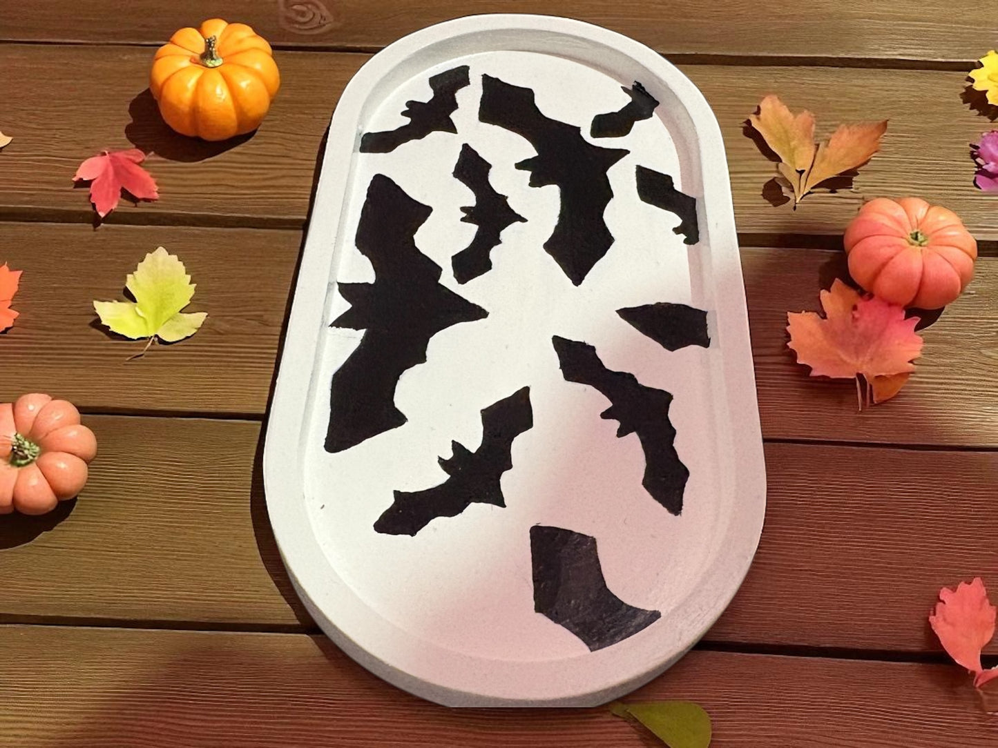 Decorative tray with black bat designs on a wooden surface with pumpkins and leaves.