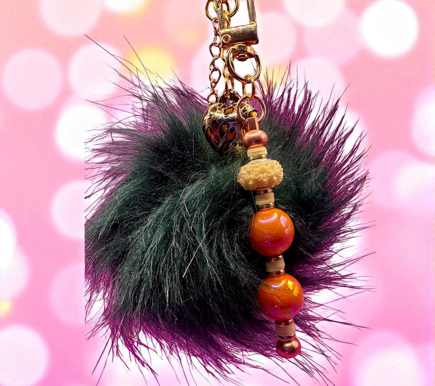 Keychain with black feathered ball and colorful beads on a pink background