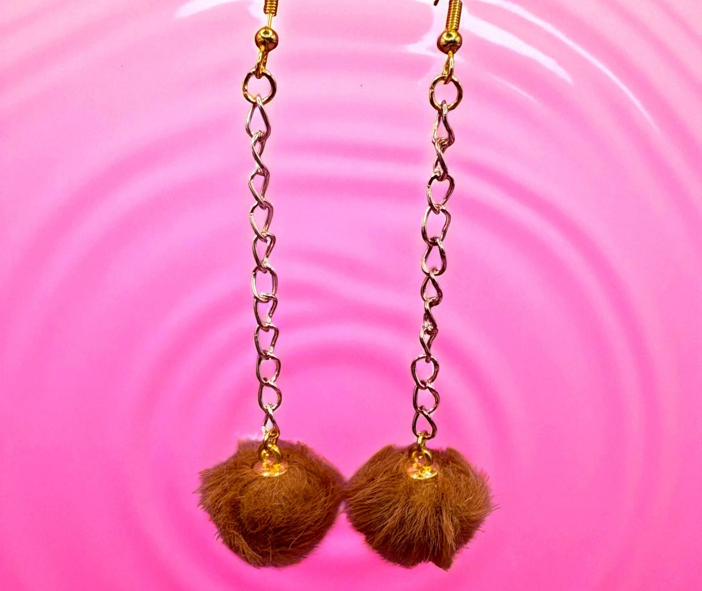 Brown pom-pom earrings with gold chains on a pink background