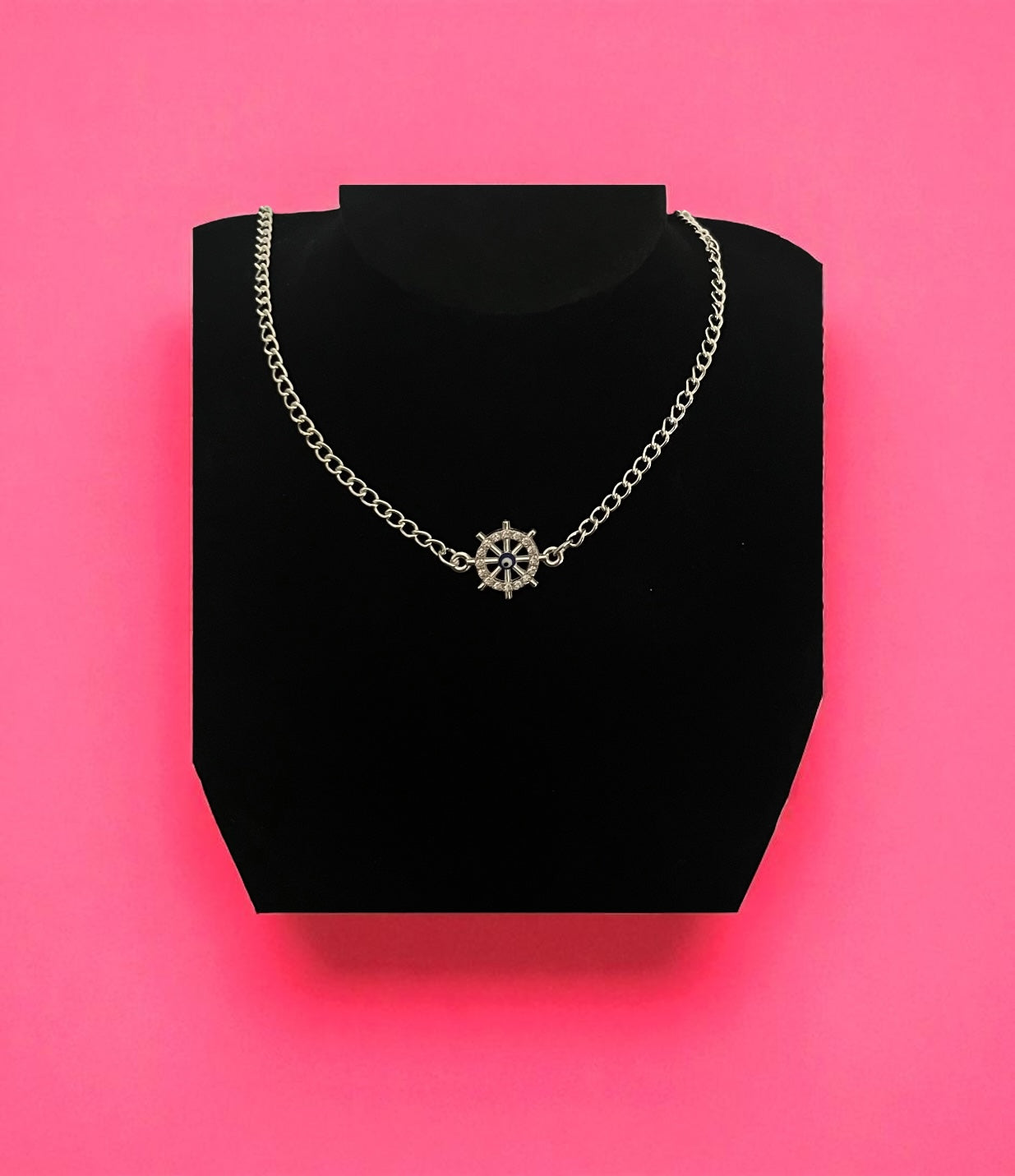 Silver necklace on a black stand against a pink background