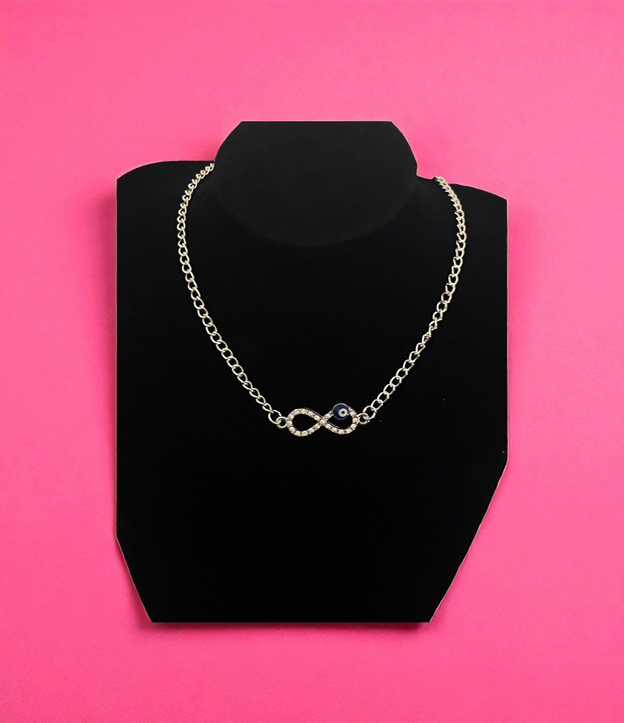 Necklace on a black stand against a pink background