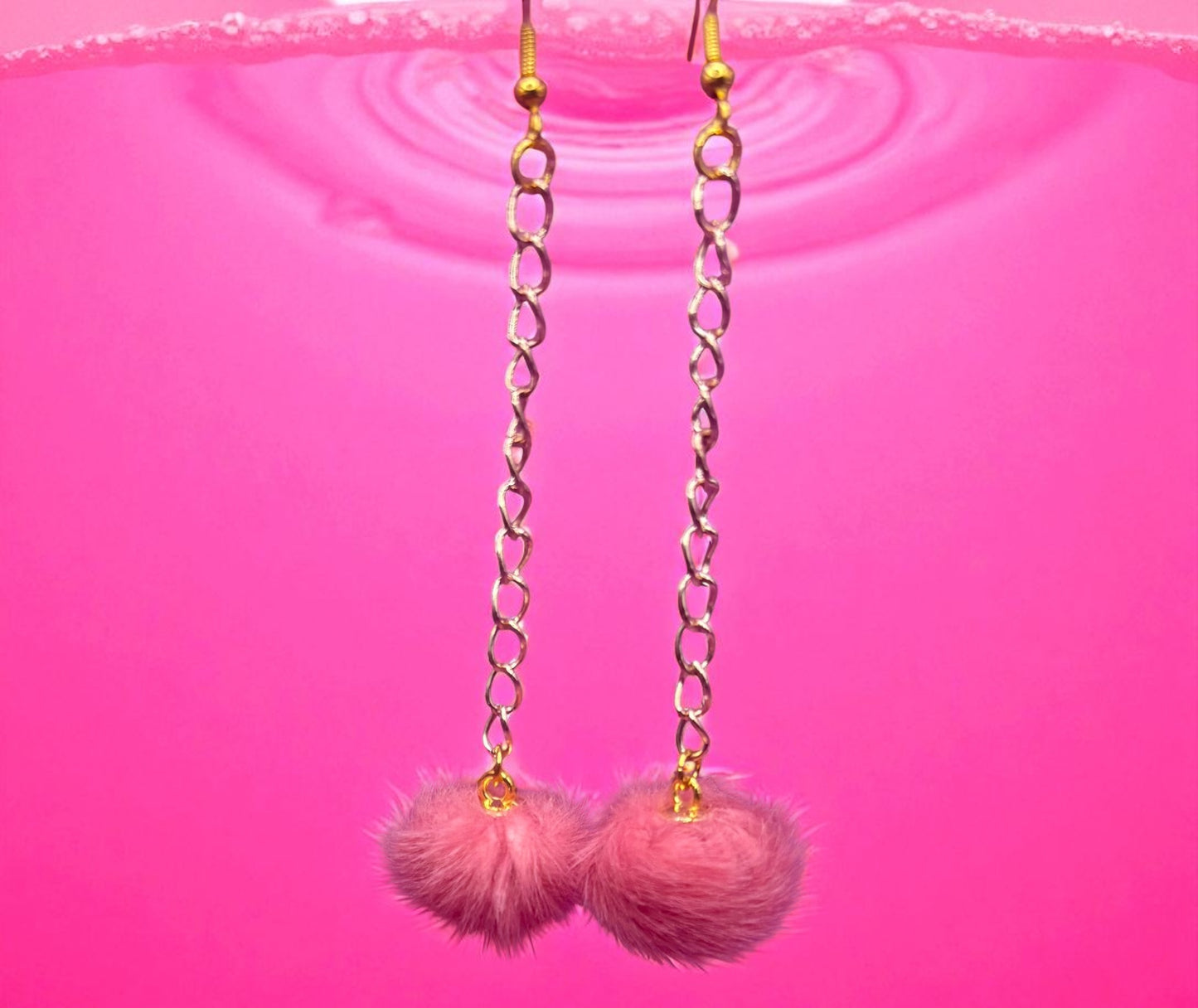 Pink pom-pom earrings with gold chains on a pink background