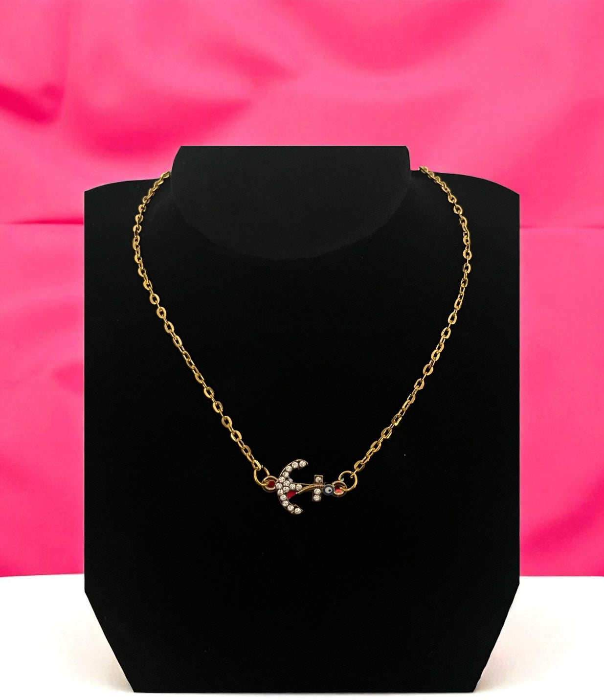 Gold necklace on a black stand with a pink background