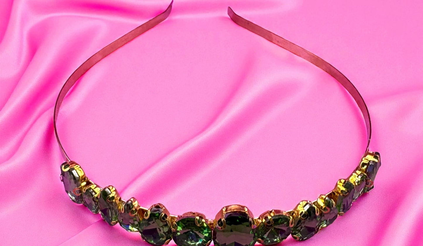 Decorative headband with green and gold stones on a pink satin background
