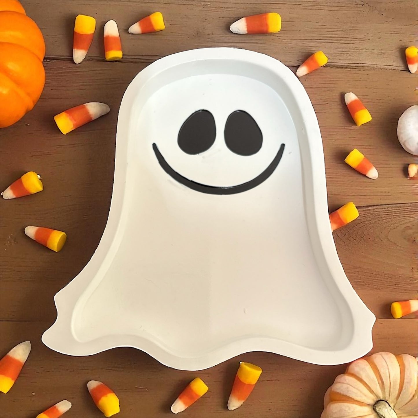 Ghost-shaped plate with candy corn and pumpkins on a wooden background