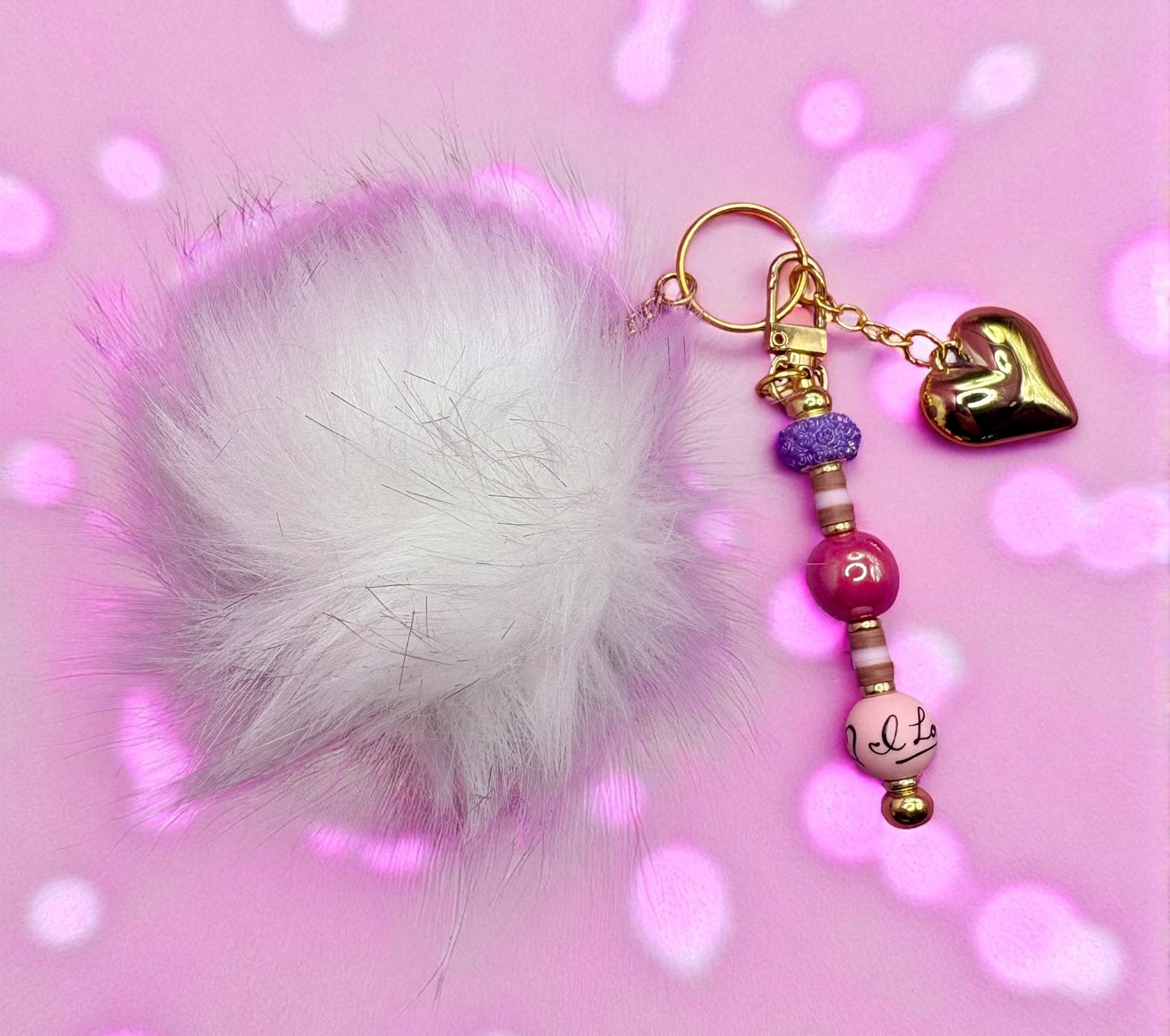 Keychain with white fluffy ball, beads, and heart charm on a pink background