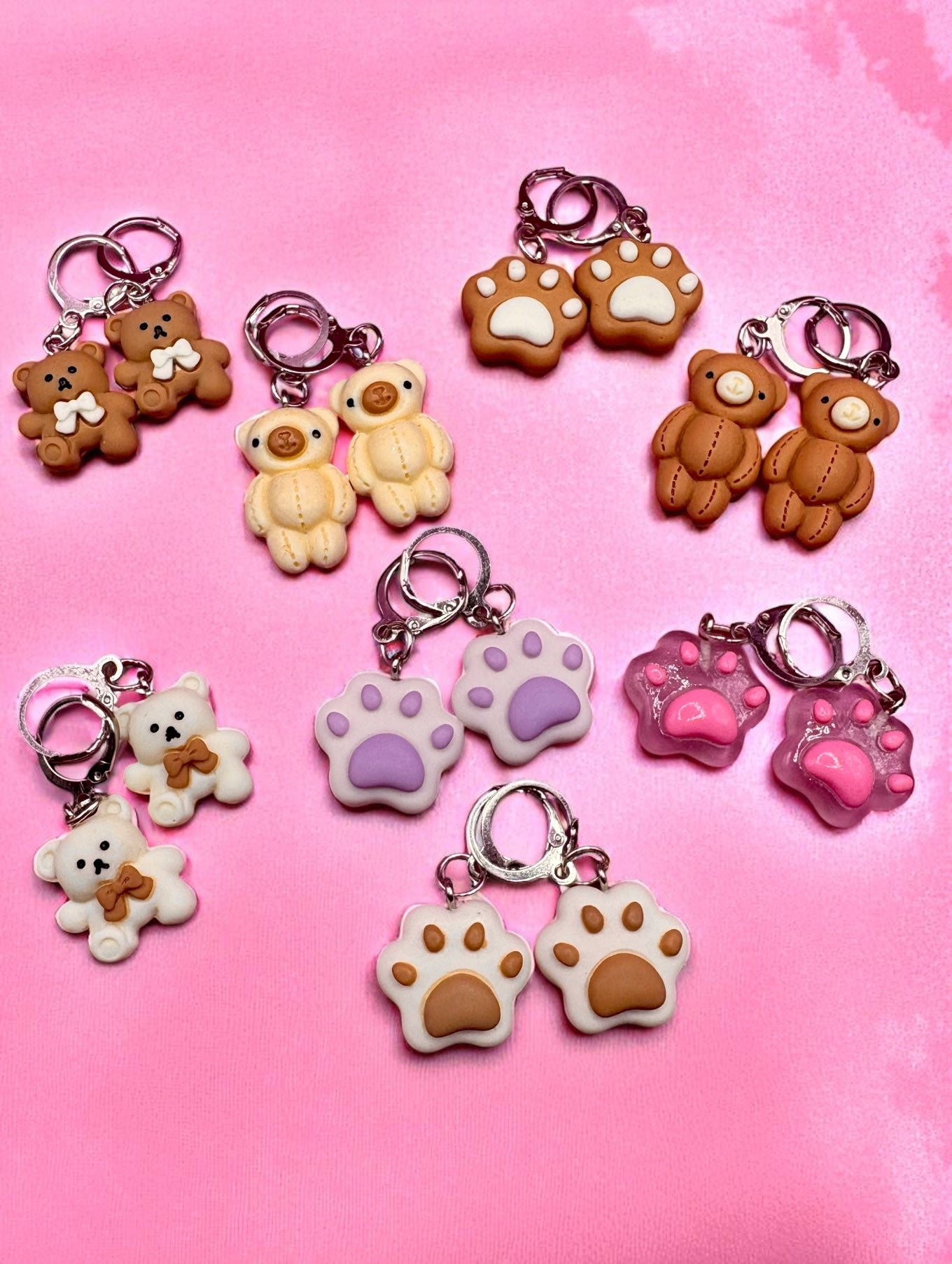 Collection of cute earrings with teddy bears and paw prints on a pink background