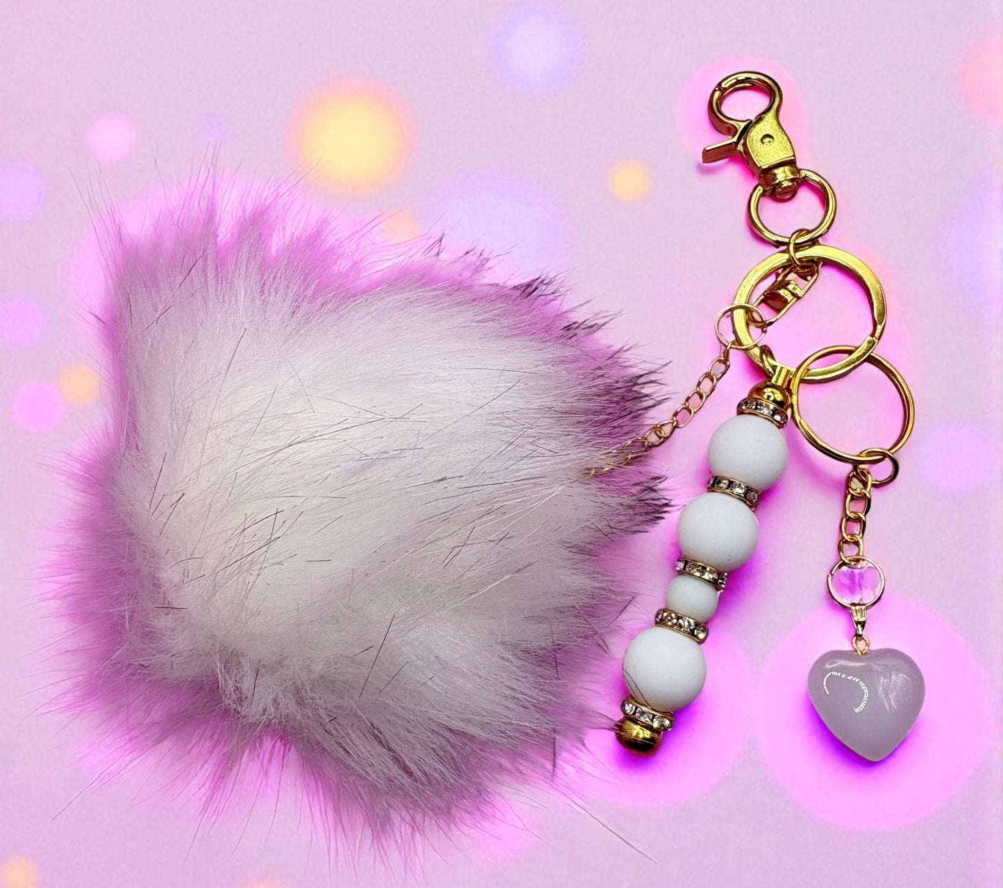 Keychain with white fluffy ball, beads, and heart charm on a pink background