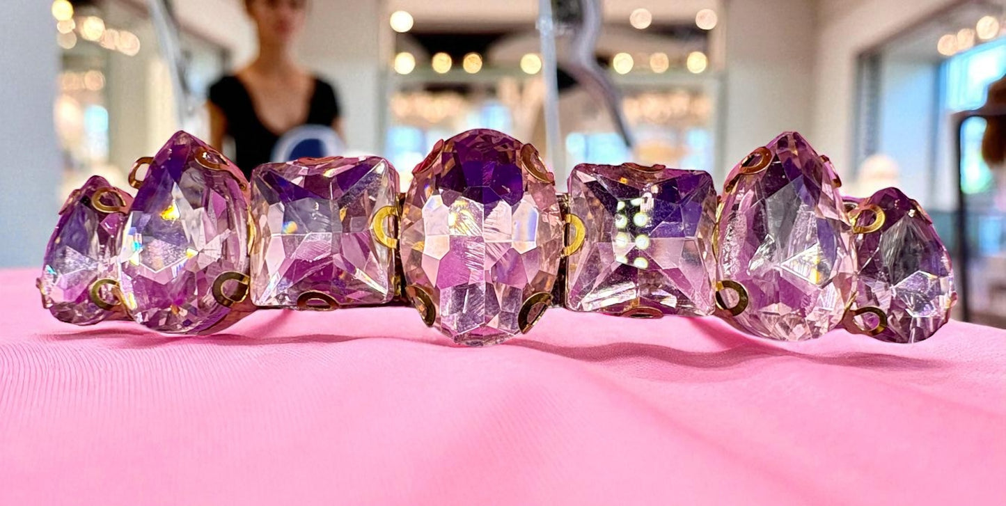 Five faceted purple gemstones hair clips on a pink surface with a blurred background
