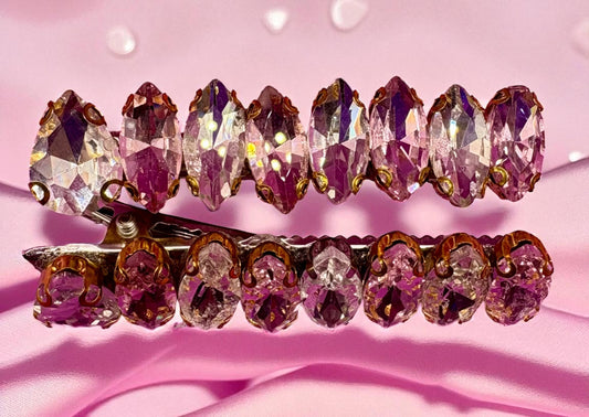 Two decorative hair clips with crystal-like beads on a pink background