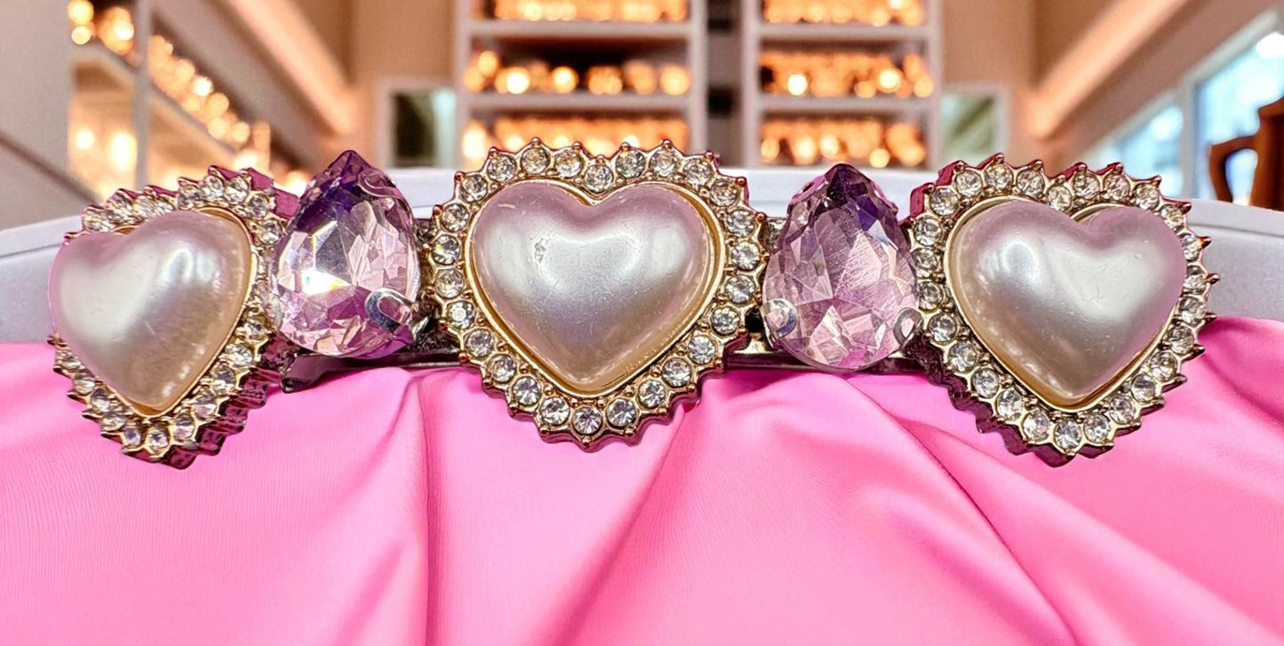 Heart-shaped hair clips with pink gemstones on a pink fabric background