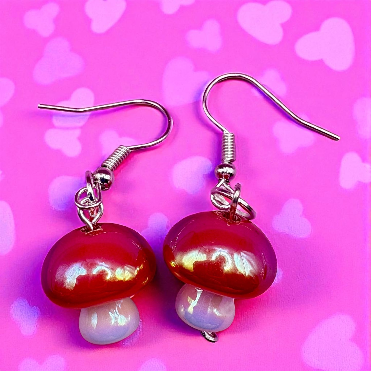 Mushroom-shaped earrings on a pink background with heart shapes