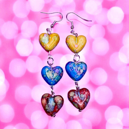 Colorful heart-shaped earrings on a pink blurred background