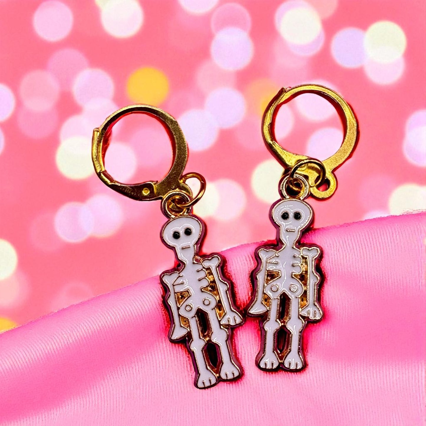Skeleton-themed earrings on a pink satin ribbon with a blurred bokeh background