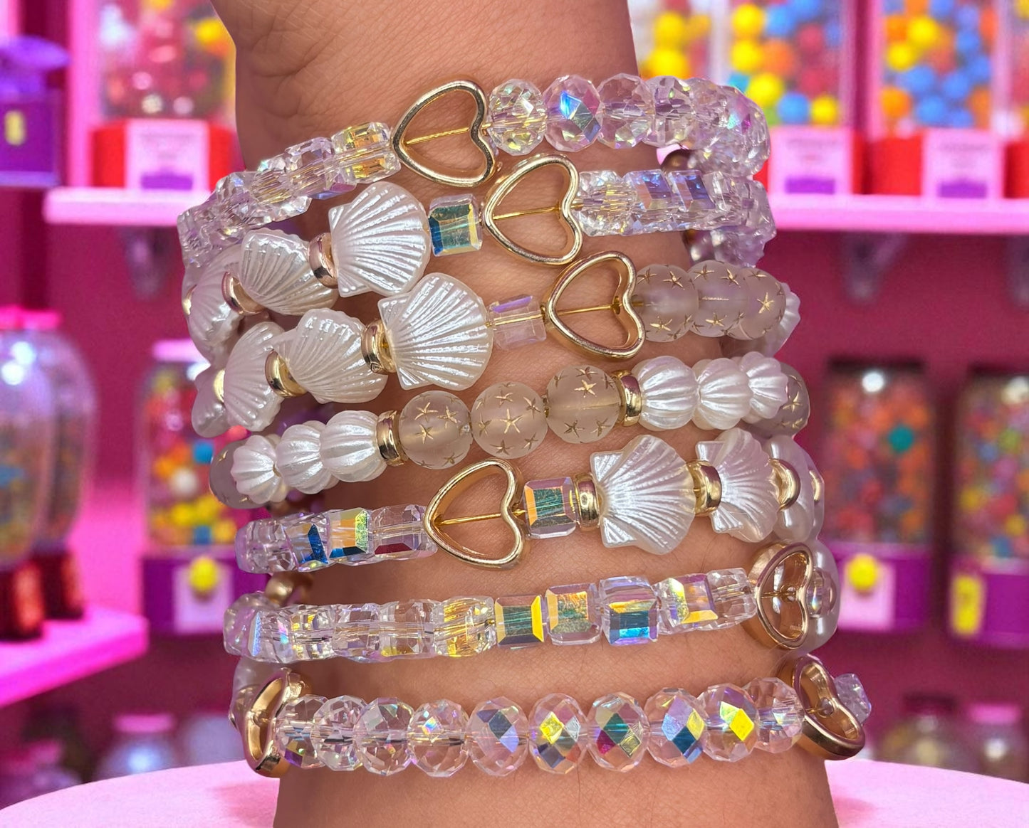 Stack of colorful beaded bracelets on a person's wrist with a pink and multicolored background.