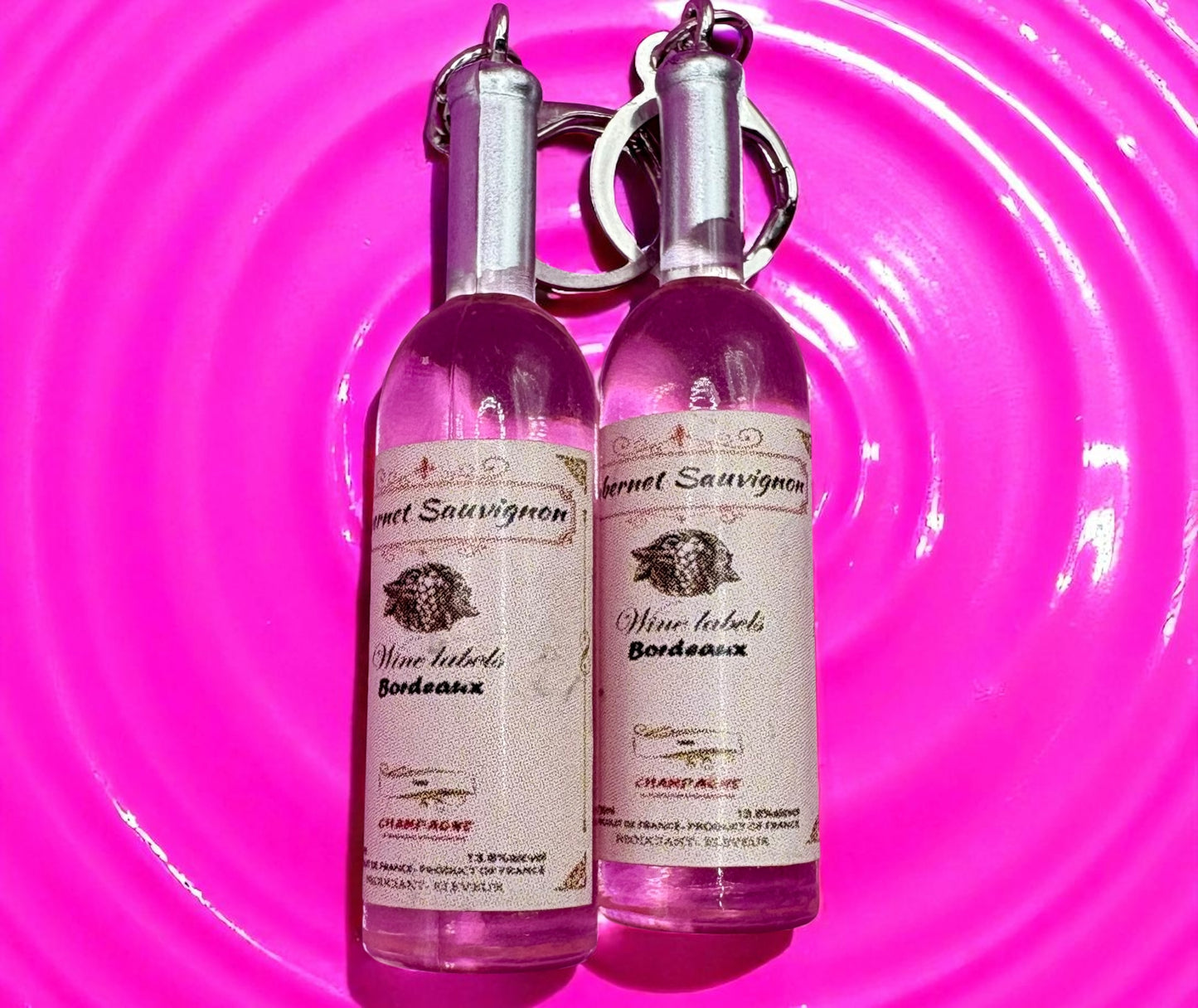 Two pink wine bottle earrings with labels on a pink circular background