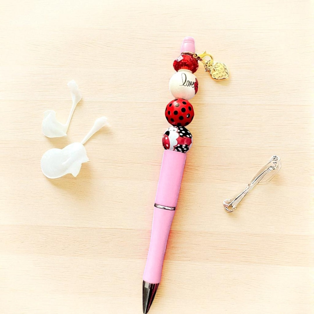 Pink pen with decorative beads on a light wooden surface