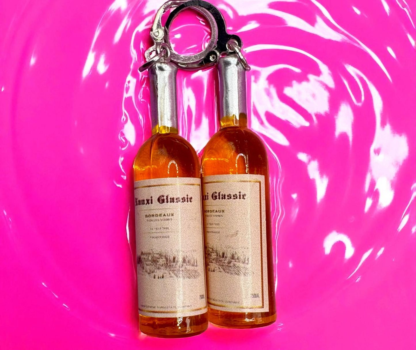 Two miniature wine bottles with labels on a pink and white swirling background