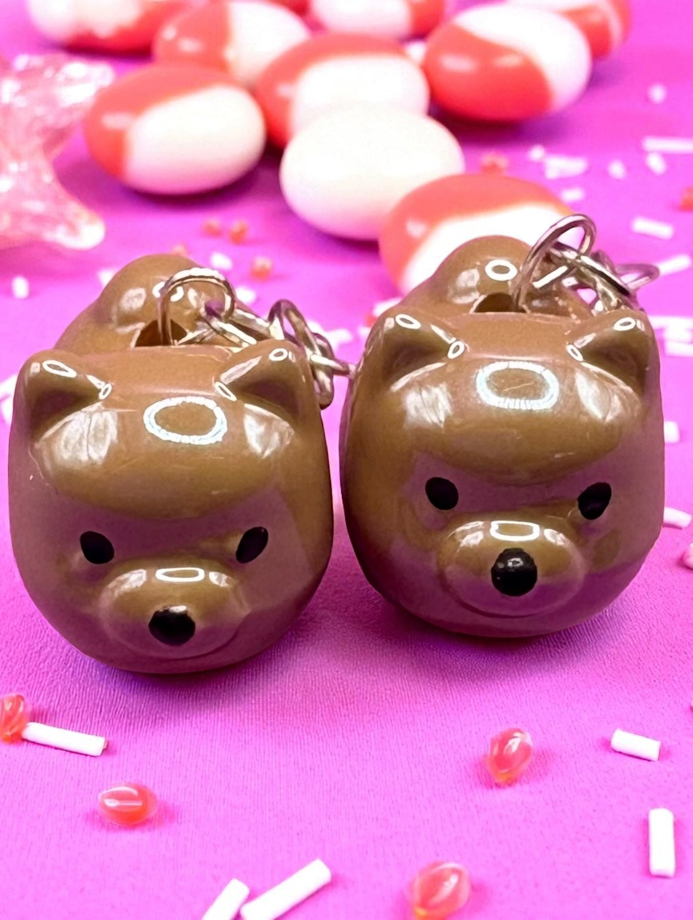 Pair of brown dog-shaped earrings on a pink background with candy decorations.