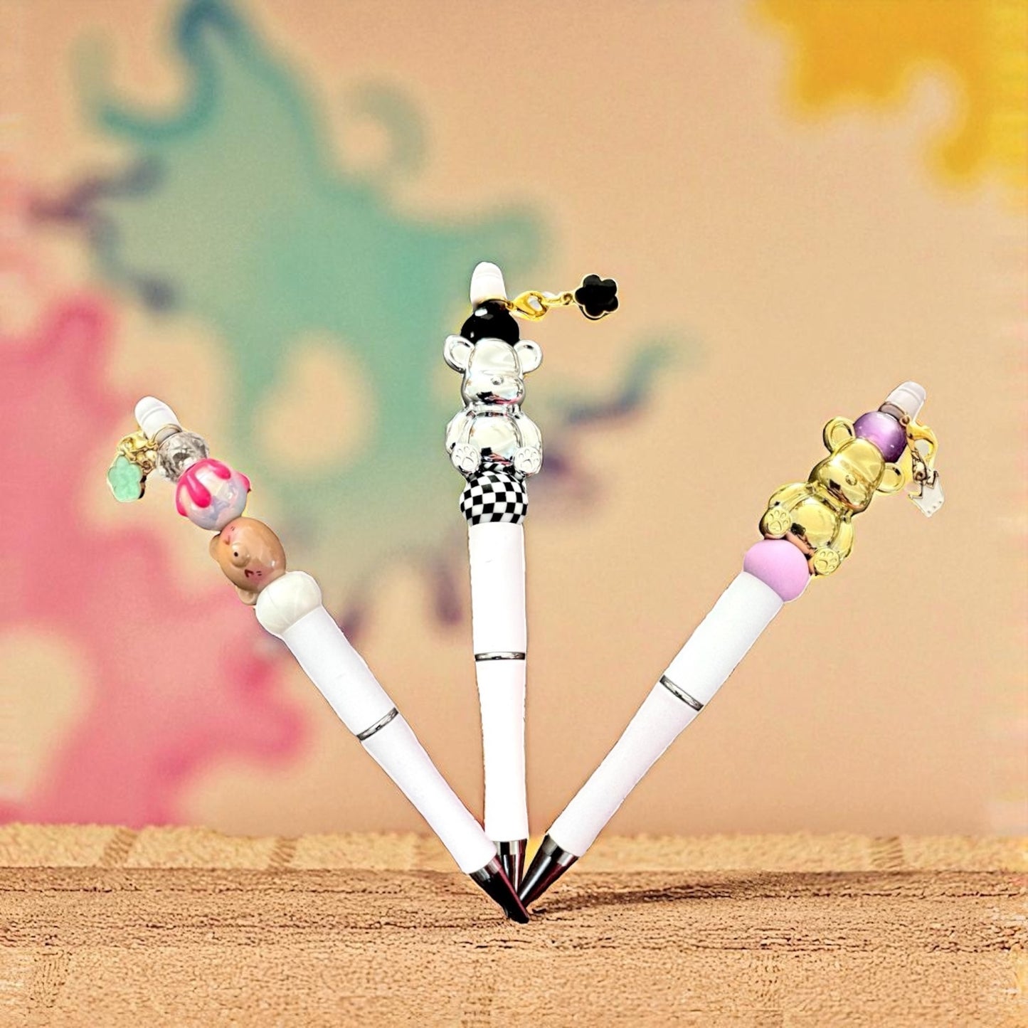 Four decorative pens with colorful bead attachments on a wooden surface.