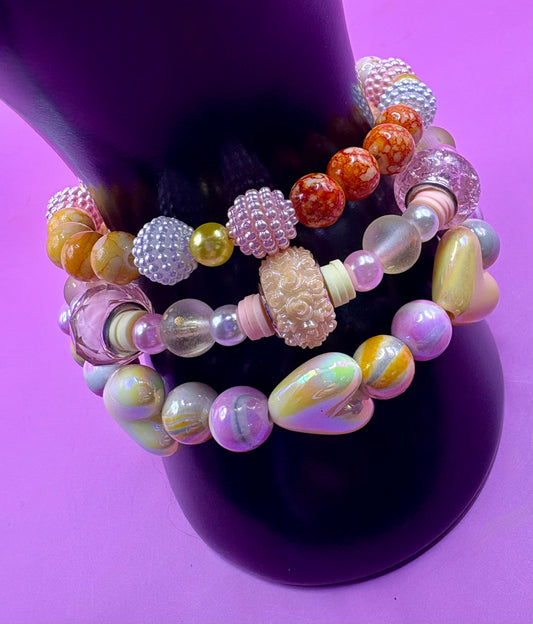 Handmade beaded charm bracelets stacked together, showcasing unique designs and vibrant colors, perfect for adding a personalized touch to any jewelry collection. yellow floral love hearts pink orange