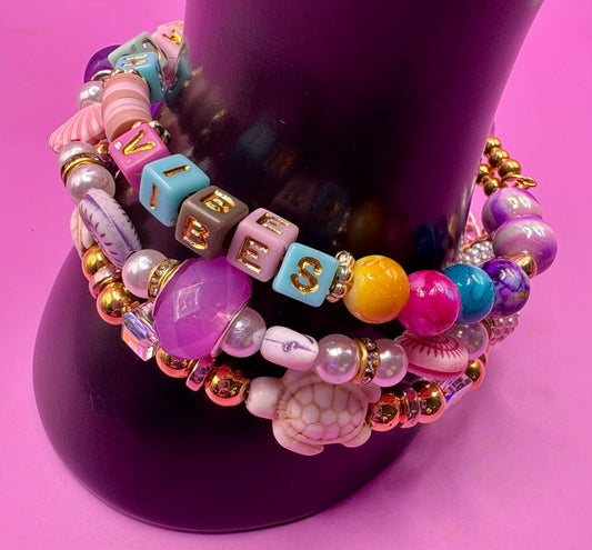 Handmade beaded charm bracelets stacked together, showcasing unique designs and vibrant colors, perfect for adding a personalized touch to any jewelry collection. beach vibes turtles seal life purple