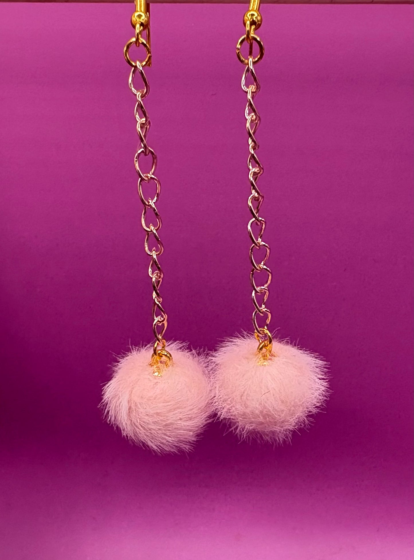 Trendy long dangly drop earrings with fluffy pom pom embellishments, perfect for adding a playful and stylish touch to your accessory collection for any occasion.