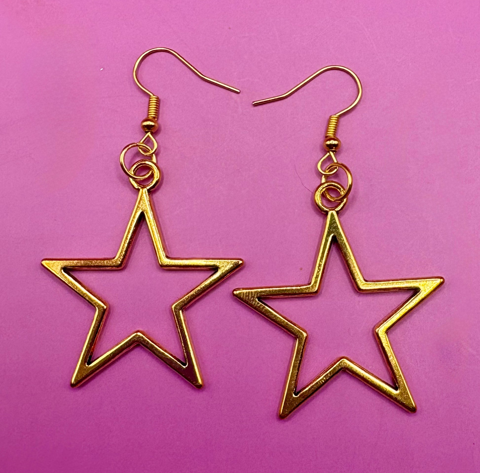 Stylish large gold star dangly earrings, featuring a bold and eye-catching design perfect for elevating any outfit with a touch of glamour and shine.