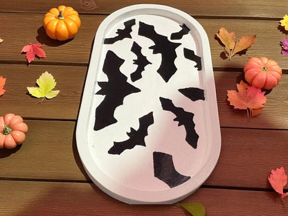 Decorative tray with black bat designs on a wooden surface with pumpkins and leaves.