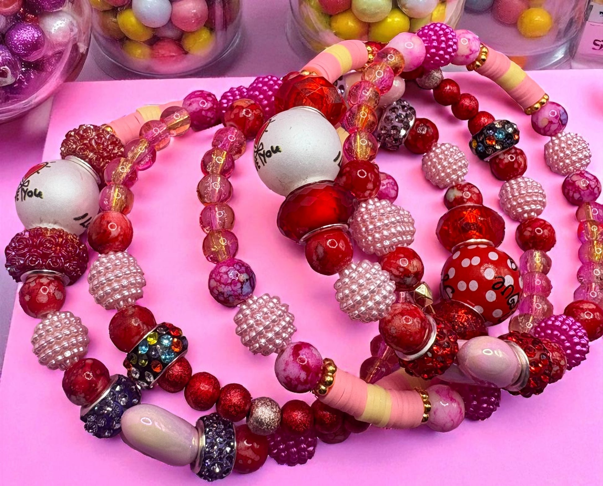 Colorful beaded necklaces on a pink surface with small containers of beads in the background.