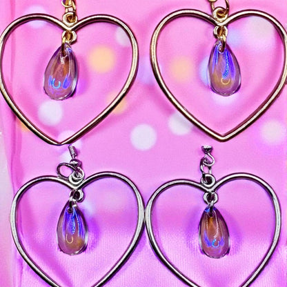Heart-shaped earrings with teardrop charms on a pink background