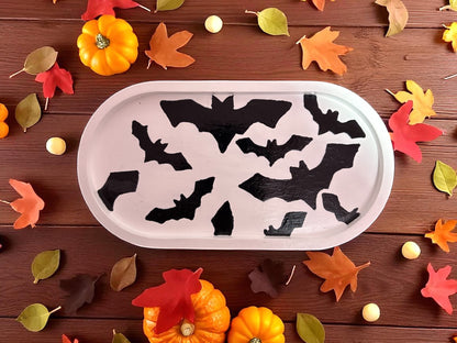 Tray with black bat shapes on a wooden surface with autumn leaves and pumpkins.