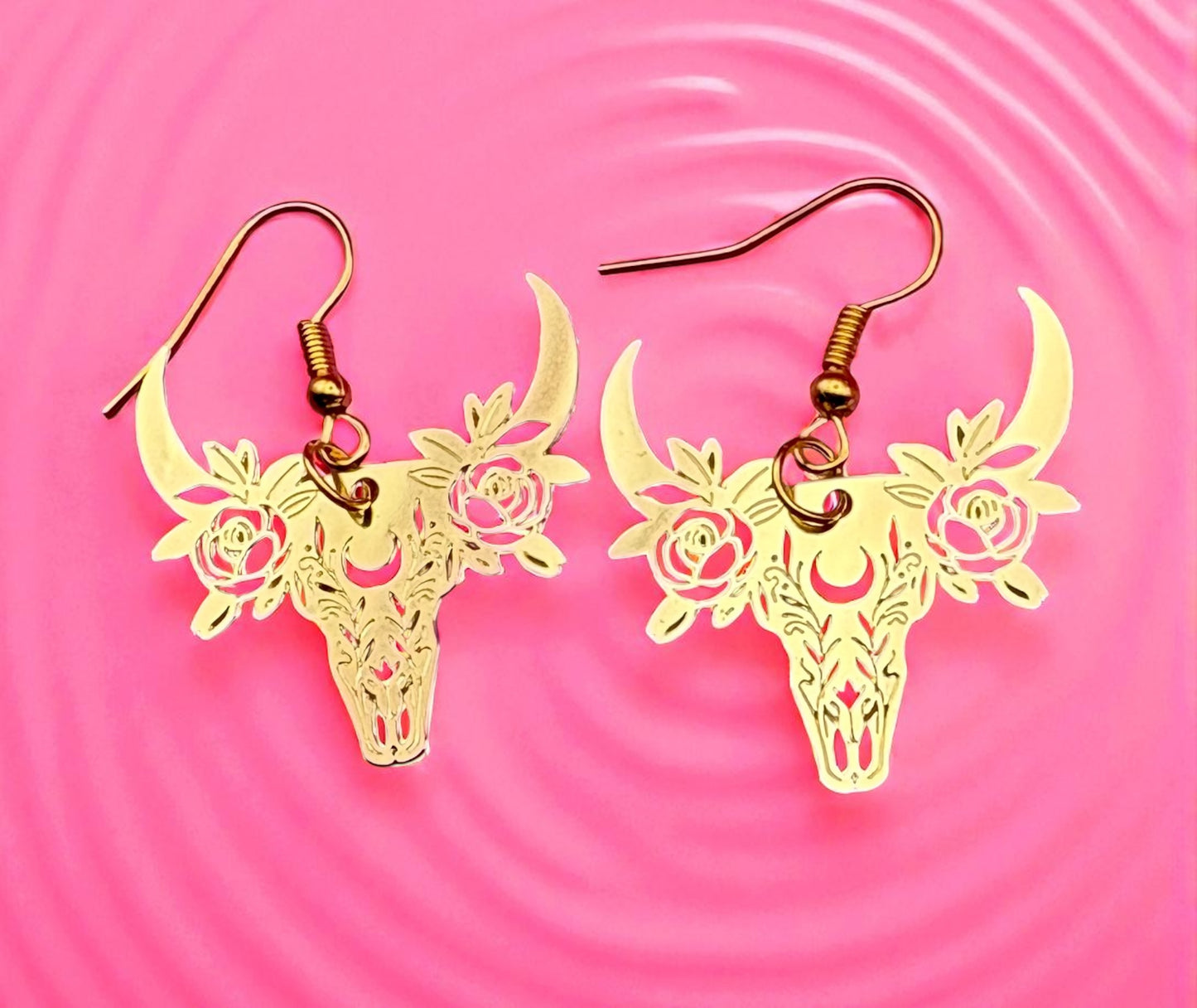 Gold deer skull earrings with floral details on a pink background