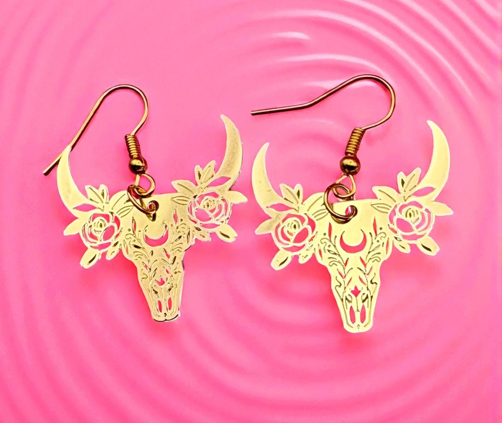 Gold deer skull earrings with floral details on a pink background