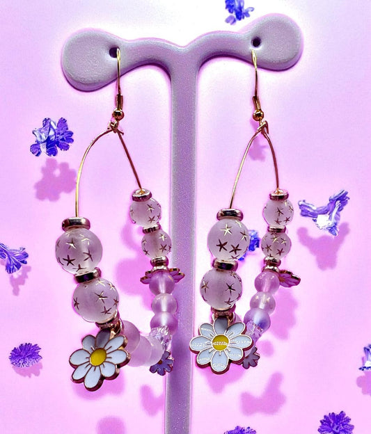 Decorative earrings with beads and floral elements on a pink background