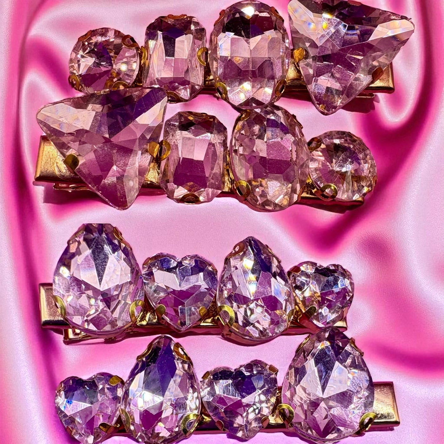 Set of three decorative hair clips with purple gemstones on a pink background