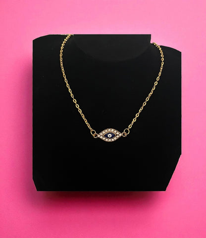 Gold necklace with an eye design on a black stand against a pink background