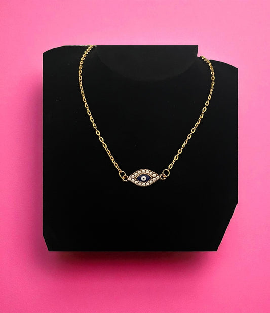Gold necklace with an eye design on a black stand against a pink background