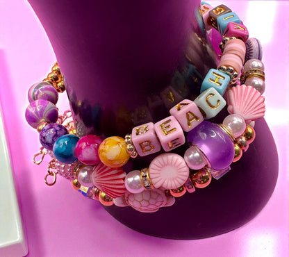 Colorful beaded bracelets with text and charms on a pink stand