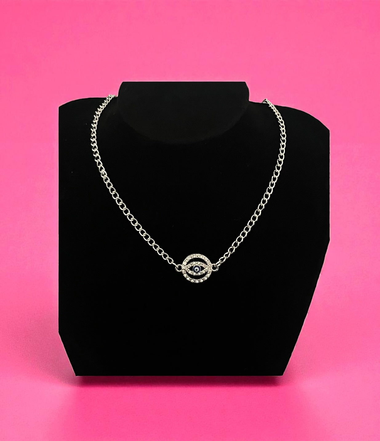 Necklace with a circular design on a black stand against a pink background
