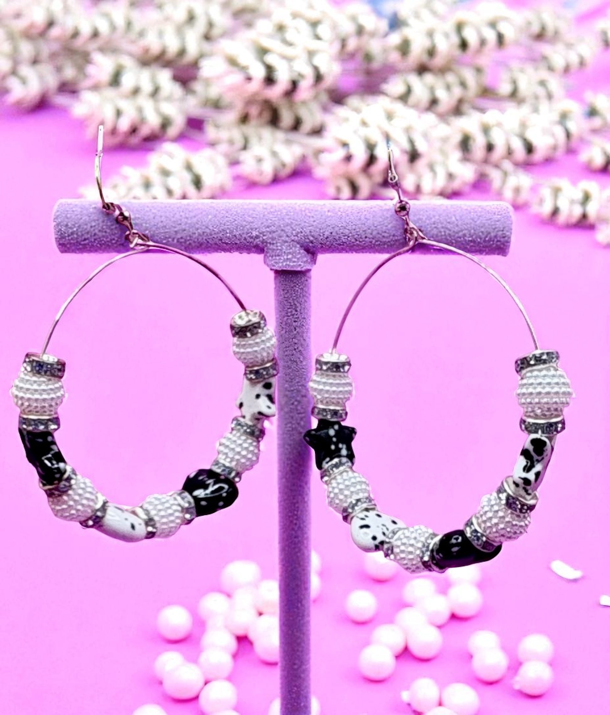 Hoop earrings with beaded design on a pink stand with white beads in the background