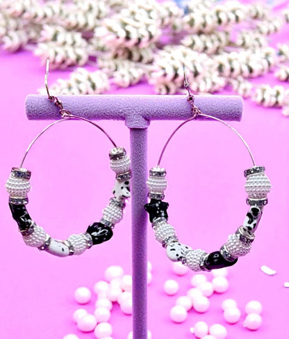 Hoop earrings with beaded design on a pink stand with white beads in the background