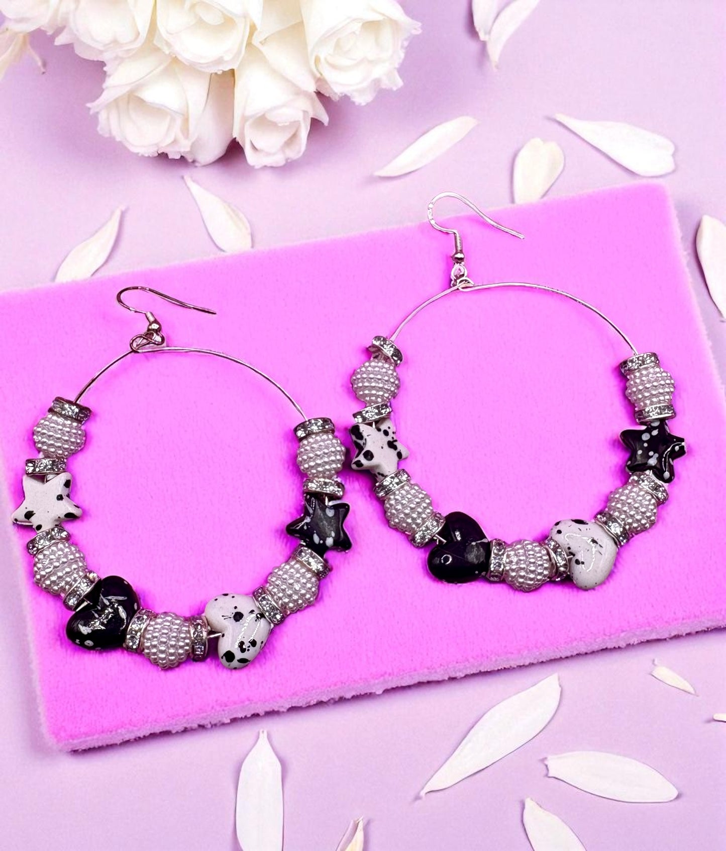 Hoop earrings with black and white bead design on a pink surface with white flowers.